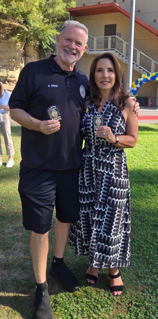 Two event attendees holding LAPD and Sunshine Kids 20th-anniversary keepsakes outdoors