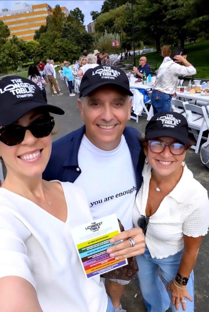 Three attendees wearing The Longest Table Stamford hats at an outdoor community gathering