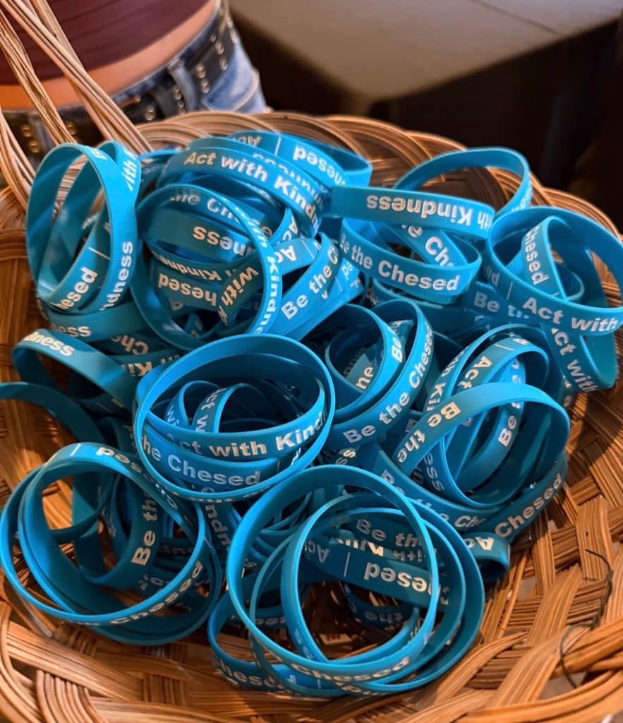 Basket of blue wristbands printed with Act with Kindness and Be the Chesed in white